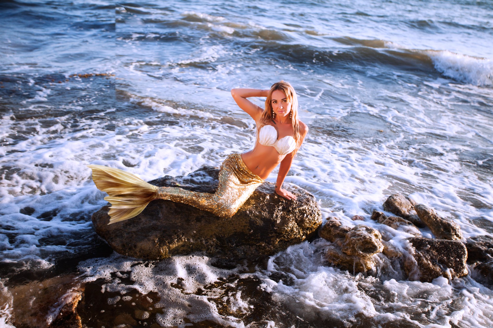 beautiful mermaid with golden tail sits on the seashore